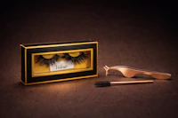 a pair of false eyelashes and a brush in a gold box