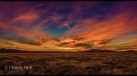 a colorful sunset over a field with mountains in the background