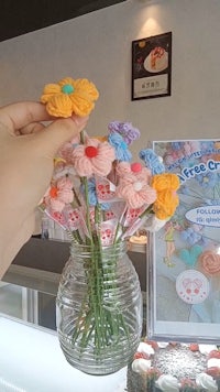 a person is holding a vase of flowers in front of a bakery