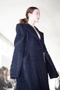 a woman walks down the runway in a black coat