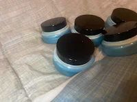 four jars of blue cream sitting on a bed