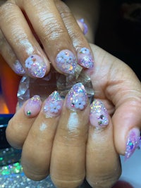 a woman holding a pink and purple glitter manicure