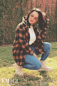 a woman crouching in the grass wearing a plaid jacket and jeans