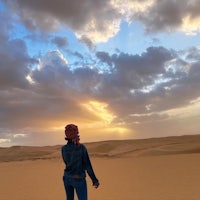 a woman standing in the desert at sunset