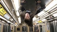 a man is hanging upside down on a subway train