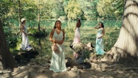 a group of women in long dresses standing near a lake