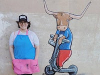 a woman in a pink apron standing next to a painting of a bull