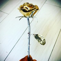 a person holding a gold rose on a wooden floor