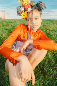 a girl sitting on a grassy field with flowers in her hair