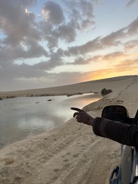 a person pointing to the water in the sand at sunset