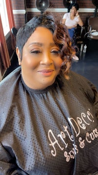 a woman in a black smock sitting in a hair salon