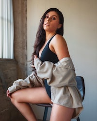a woman sitting on a chair wearing a black jacket and black shorts