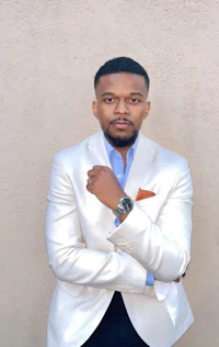 a man in a white suit leaning against a wall