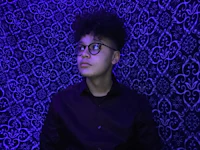 a young man wearing glasses and a black shirt in front of a purple wall