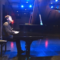 a young man playing a grand piano in a dark room