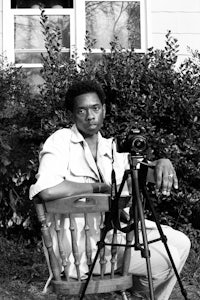 a black and white photo of a man sitting in a chair with a camera
