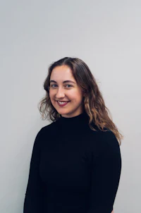 a woman in a black turtle neck top smiling against a white wall