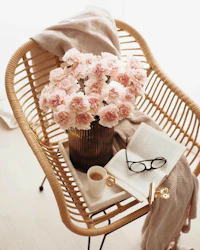 a rattan chair with a vase of pink flowers and a book