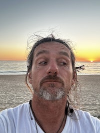 a man with long hair taking a selfie on the beach