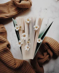 a book with flowers and a sweater on a marble table