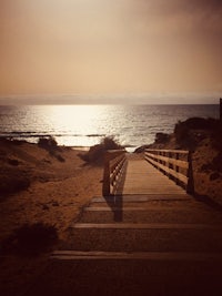 a wooden walkway leading to the beach at sunset