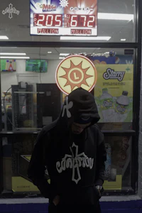 a man in a black hoodie standing in front of a store