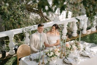 a bride and groom sitting at a table in a garden