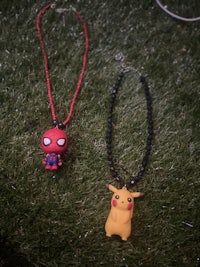 two spider - man and pikachu necklaces on grass