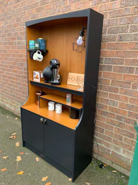 a black cabinet with a coffee maker and mugs