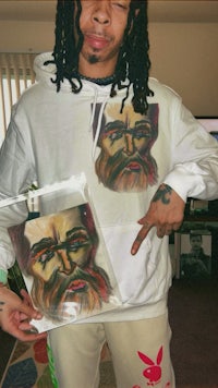 a man with dreadlocks holding a hoodie with a painting on it