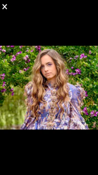 a woman in a purple dress is standing in front of flowers