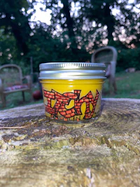 a yellow jar with graffiti on it sits on a wooden stump