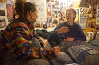 two people laughing on a bed in a dorm room