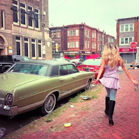 a woman walking down a street with a car in the background