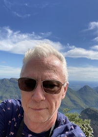 a man in sunglasses taking a selfie at the top of a mountain
