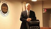 a man in a suit standing in front of a chair