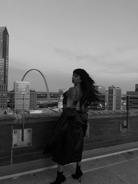 a black and white photo of a woman standing on a rooftop with the st louis arch in the background
