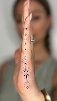 a woman's hand with a black henna tattoo on it