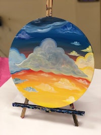 a painting of a sunset with clouds on an easel