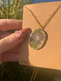 a hand holding a necklace with a flower on it