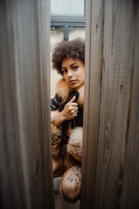 a woman in a fur coat peeking out of a wooden door
