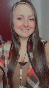 a woman with long brown hair and a plaid vest