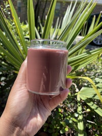 a hand holding a glass candle in front of a palm tree