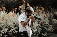 a man holding a camera in front of flowers