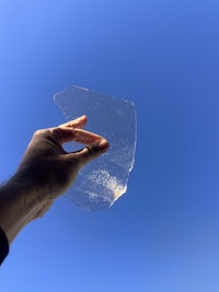 a person holding a piece of clear plastic against a blue sky