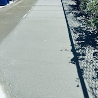 a person riding a bike on a sidewalk next to a fence