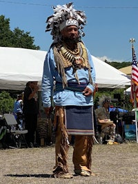 a man in a native headdress standing in front of a tent