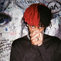 a man with red and black dreadlocks in front of a graffiti wall