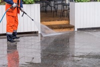 a man spraying a sidewalk with a hose