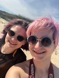 two women with pink hair taking a selfie on the beach